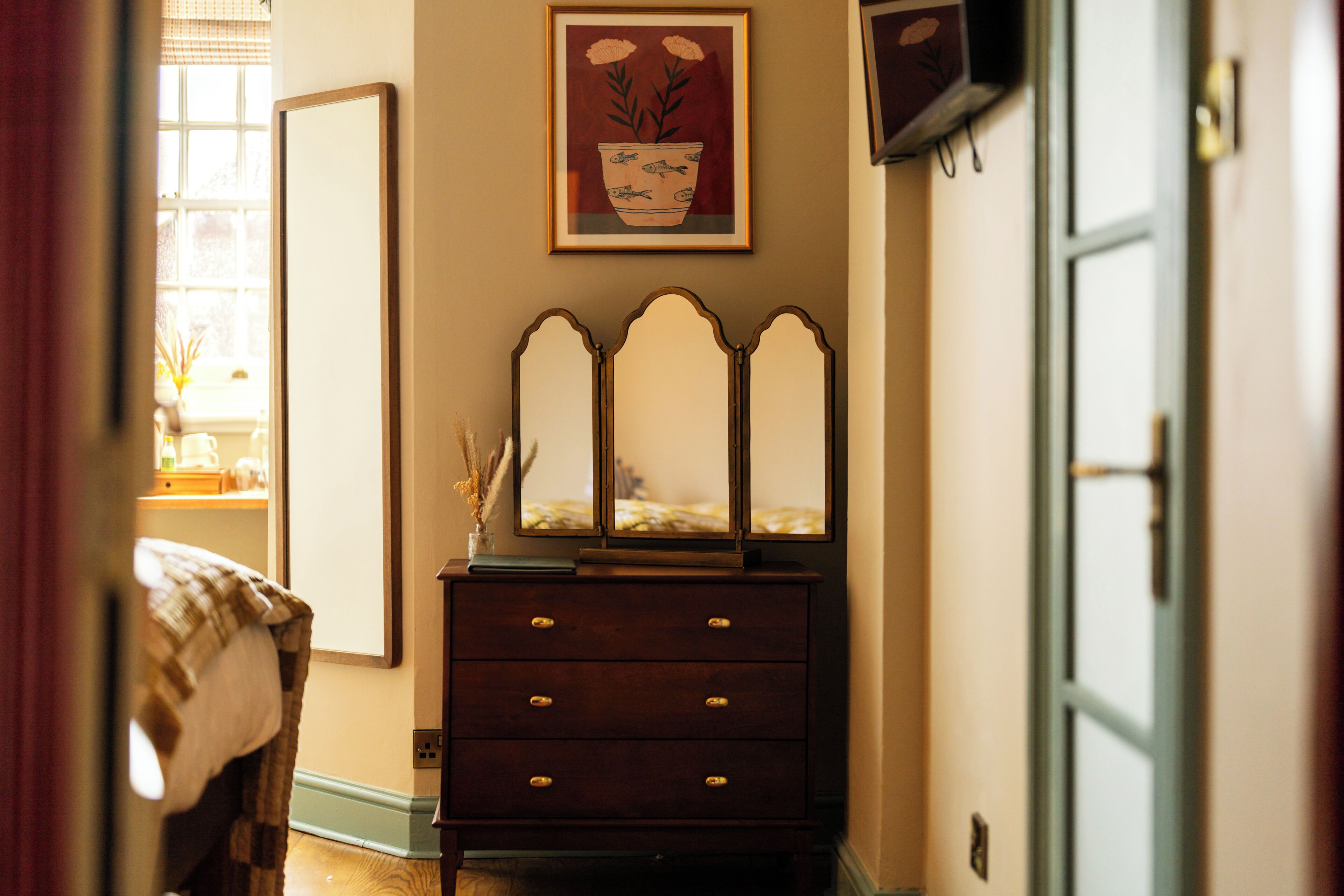 A room with a dresser, a mirror, and a framed artwork on the wall.