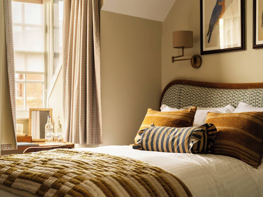 A neatly made bed with striped bedding, a bedside table with a lamp, and a window with curtains.