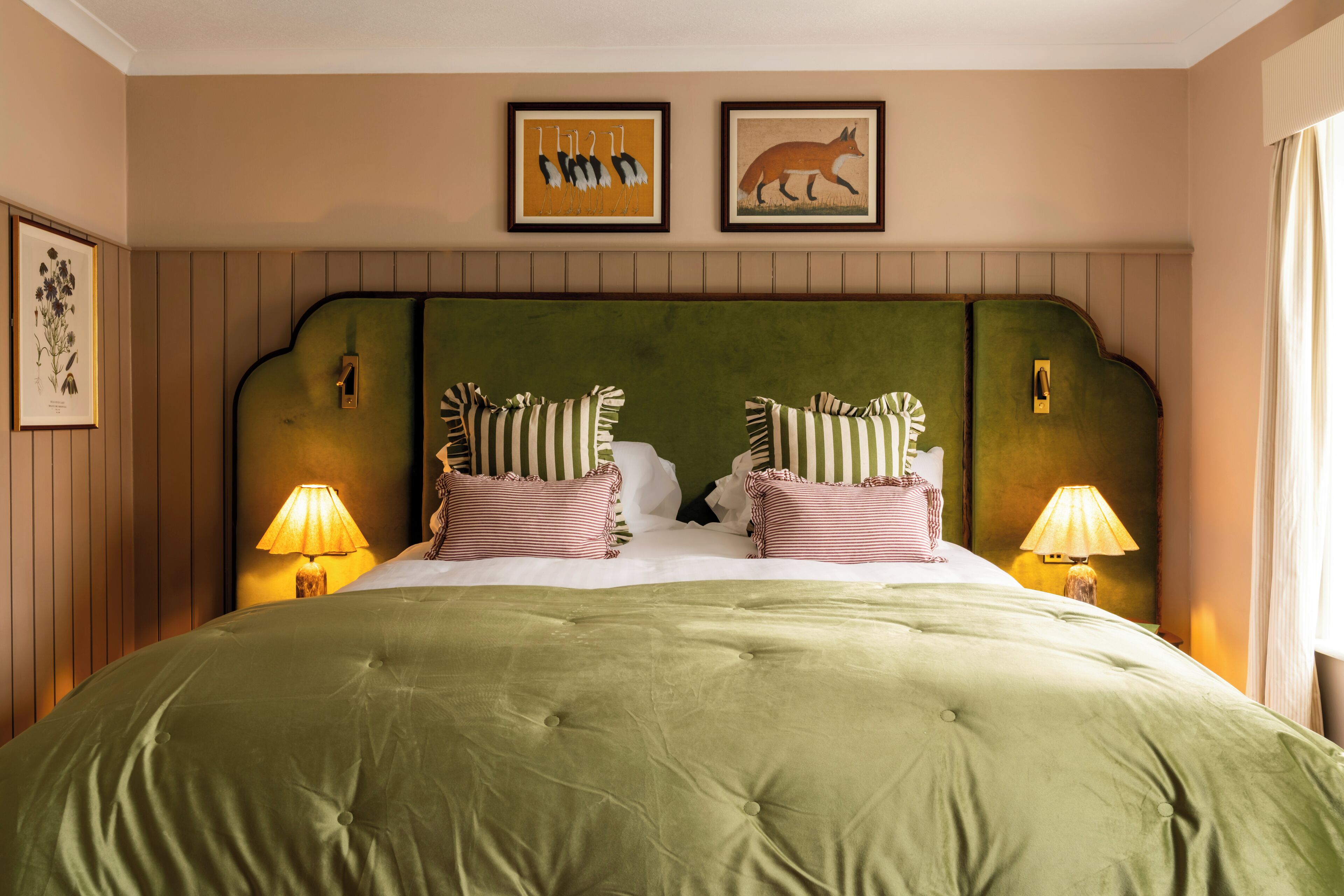 Una cama con cabecera tapizada en verde, almohadas a rayas y dos lámparas fijadas a la pared.