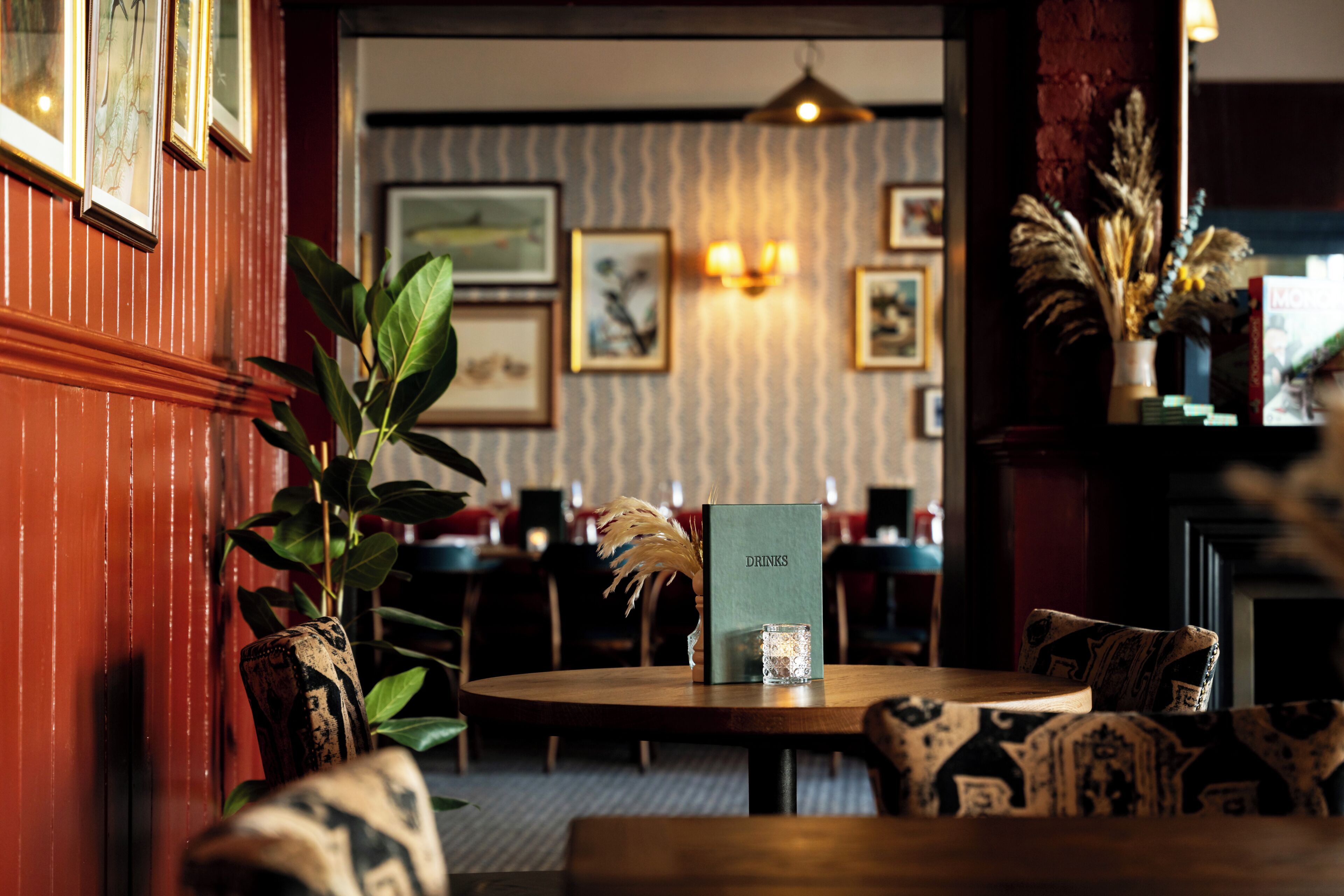 A restaurant interior with a wooden table, chairs, a menu stand, and framed artwork on the walls.