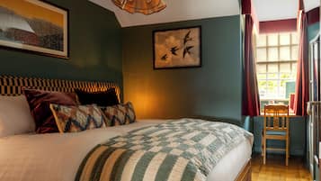 A bedroom with a bed, pillows, a framed picture, a window with curtains, and a chair.
