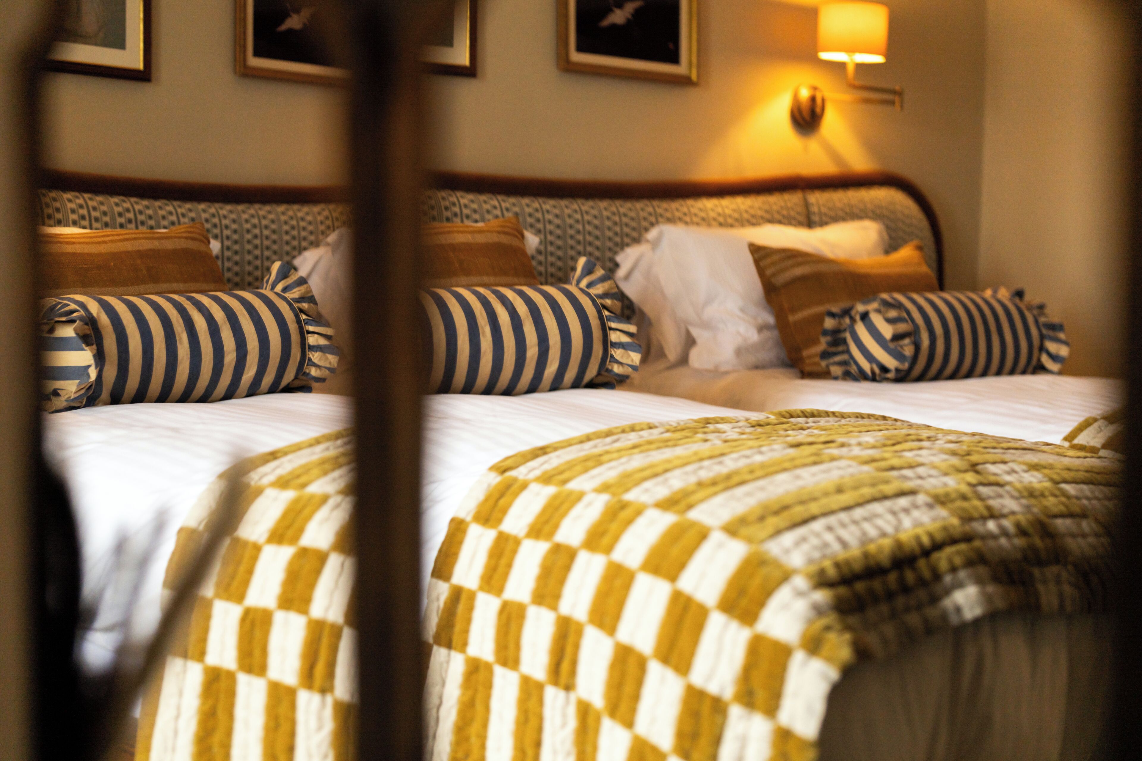 A hotel room with a bed, pillows, and a wall-mounted lamp.