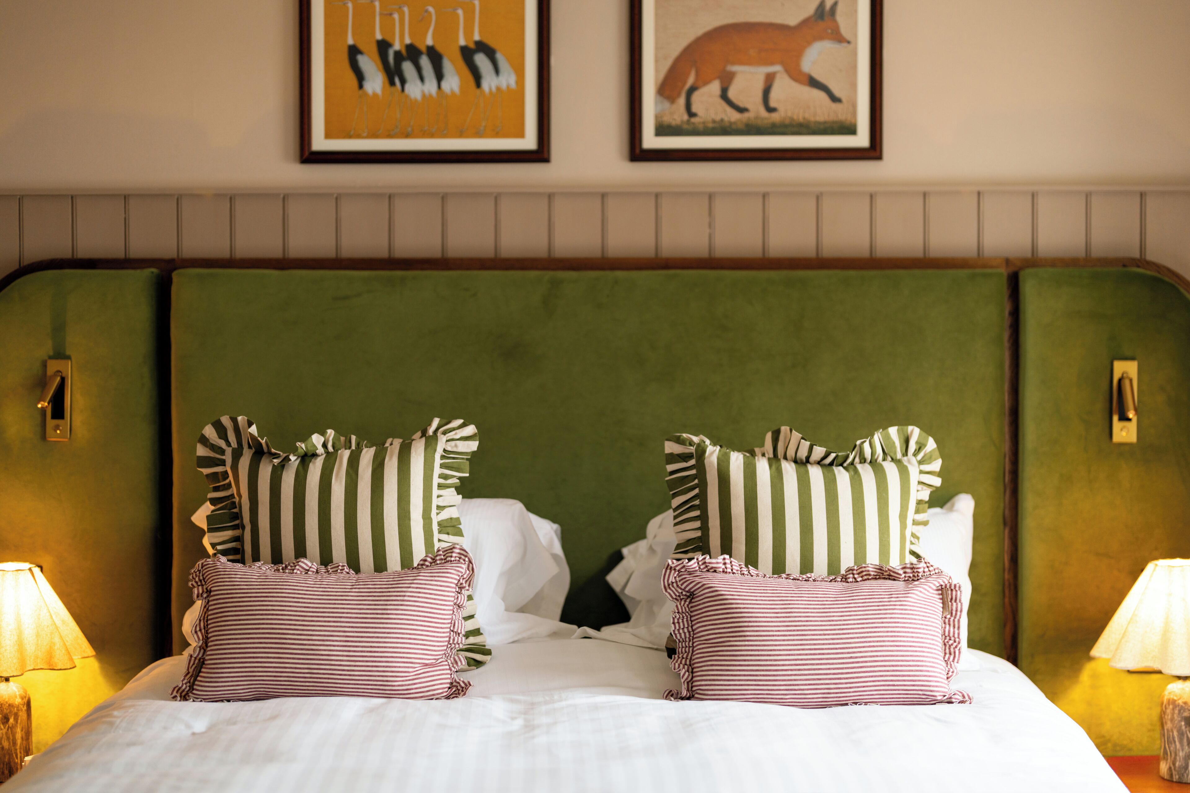 A bed with striped pillows, a green headboard, and two framed pictures on the wall.