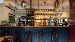 A bar area with stools, a counter with a variety of bottles, glasses, and a cash register. - The Swan (Arundel)