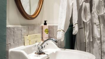 A bathroom with a white sink, a mirror, and a rack with white robes.