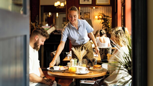 A restaurant interior with a waiter serving food to guests at a round table. - The Swan (Arundel)