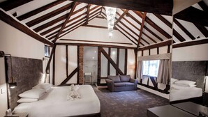 A spacious bedroom with a large bed, a sofa, and a desk. The room features exposed wooden beams and a chandelier. - Best Western Brome Grange (Eye)