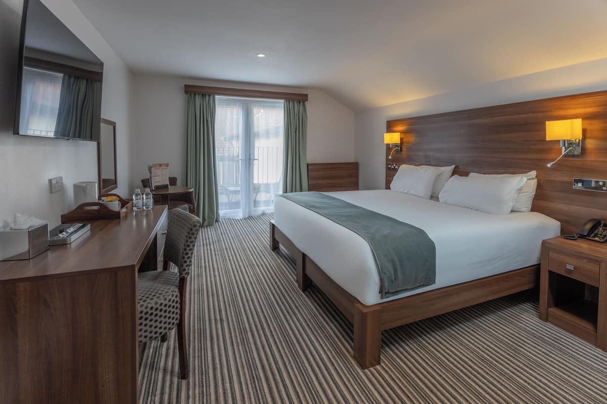 A hotel room with a large bed, a desk, a chair, a desk lamp, and a nightstand.
