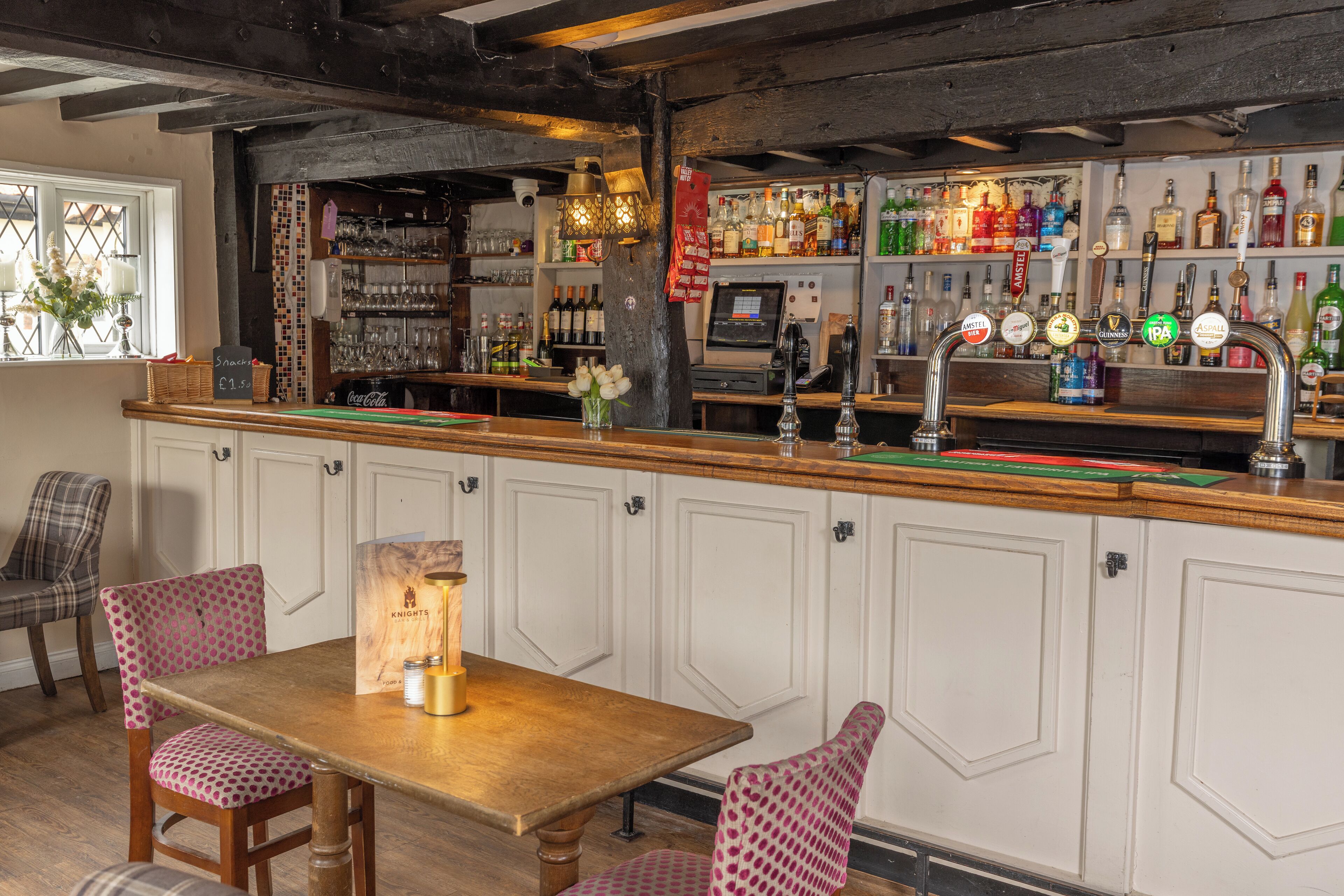 A bar area with a wooden counter, bar stools, and shelves stocked with various bottles.