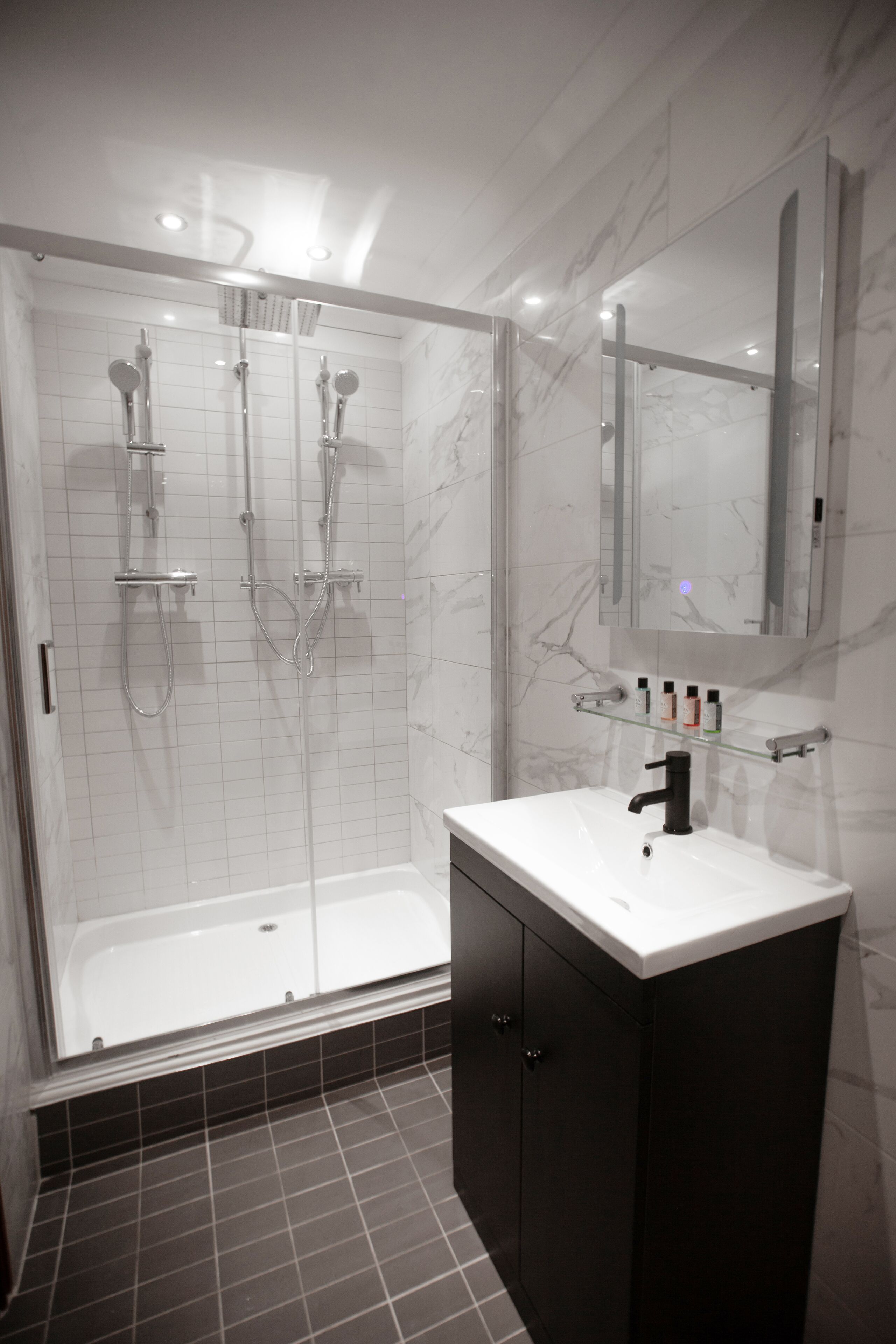 Un bagno moderno con cabina doccia in vetro, un lavandino bianco e un mobile contenitore scuro.