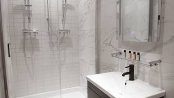 Un bagno moderno con cabina doccia in vetro, un lavandino bianco e un mobile contenitore scuro.
