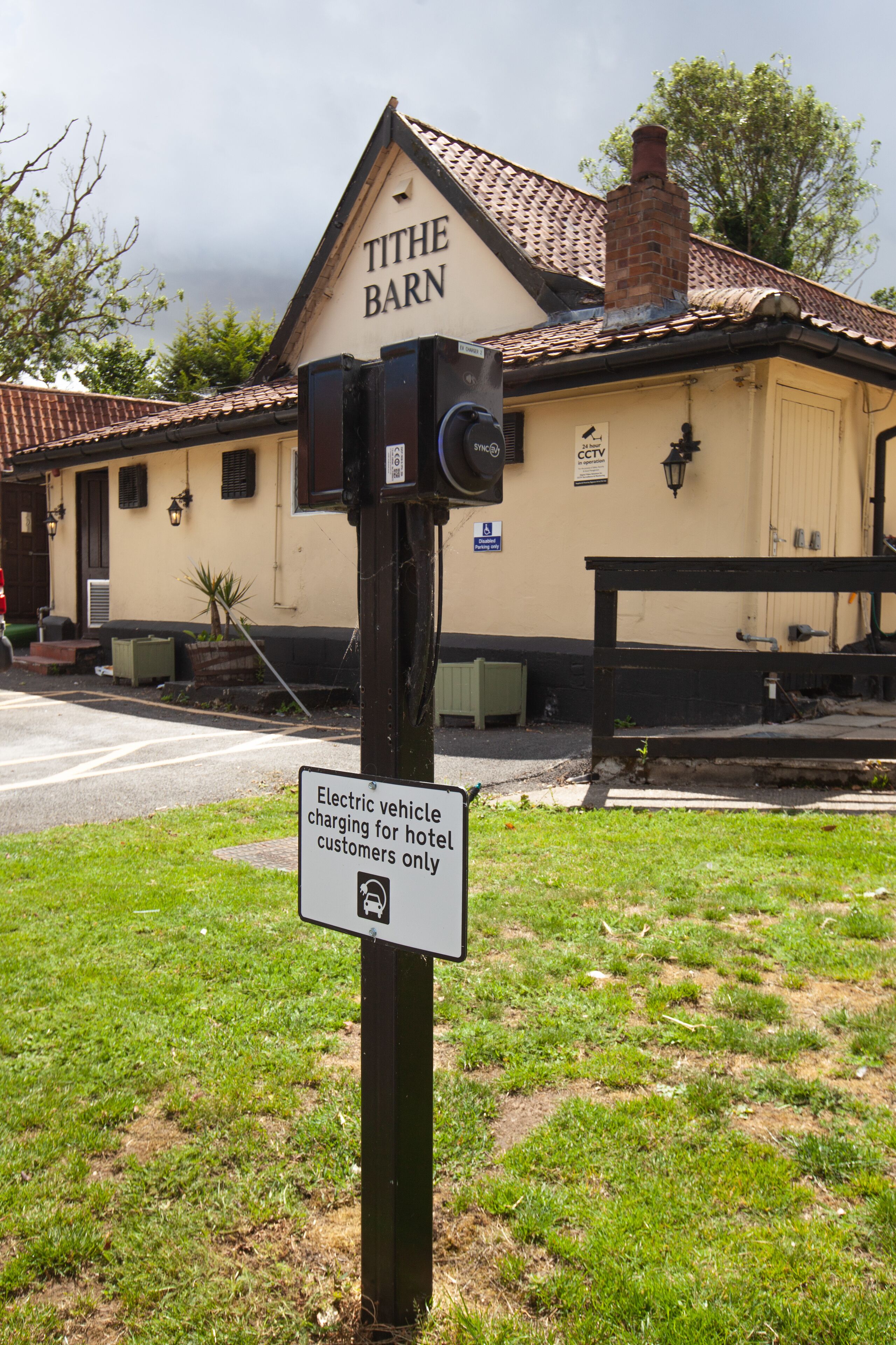 A sign for electric vehicle charging at The Barn hotel, with a brick building in the background.