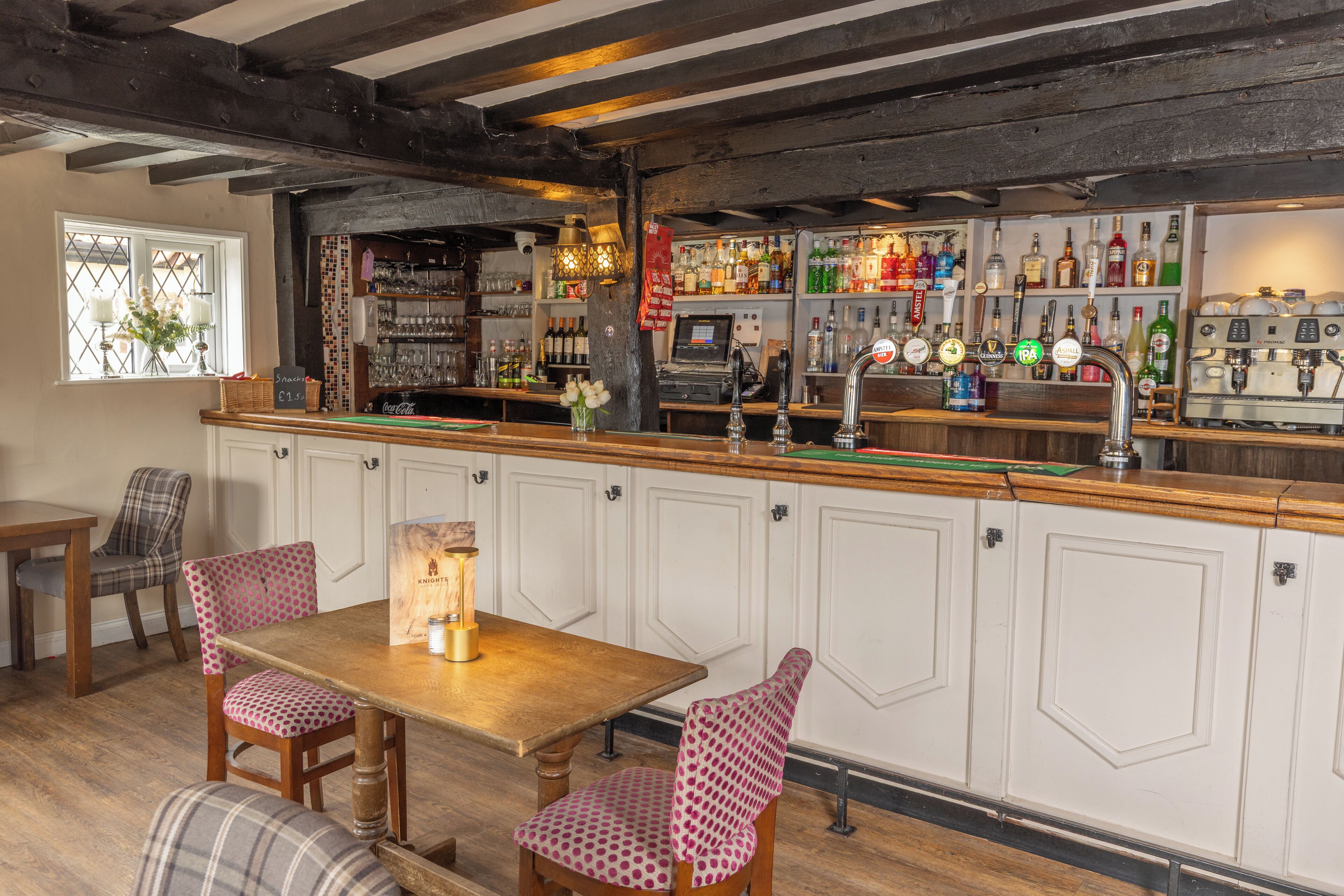 A bar area with wooden furniture, a bar counter, and shelves with various bottles.