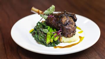 A plate of food with a lamb shank, greens, and mashed potatoes.