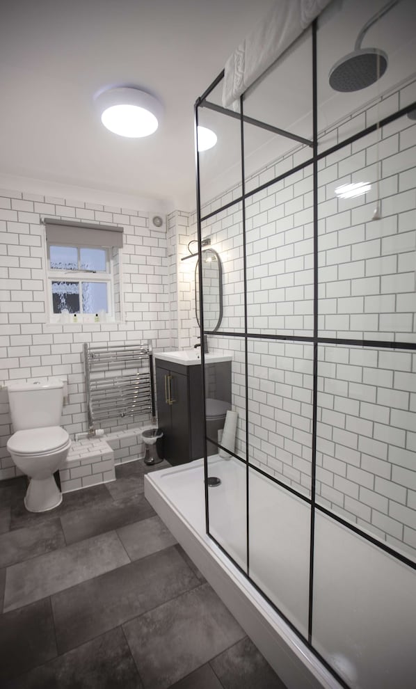 A modern bathroom with white subway tiles, a glass shower enclosure, a toilet, a sink, and a window. - Best Western Brome Grange (Eye)