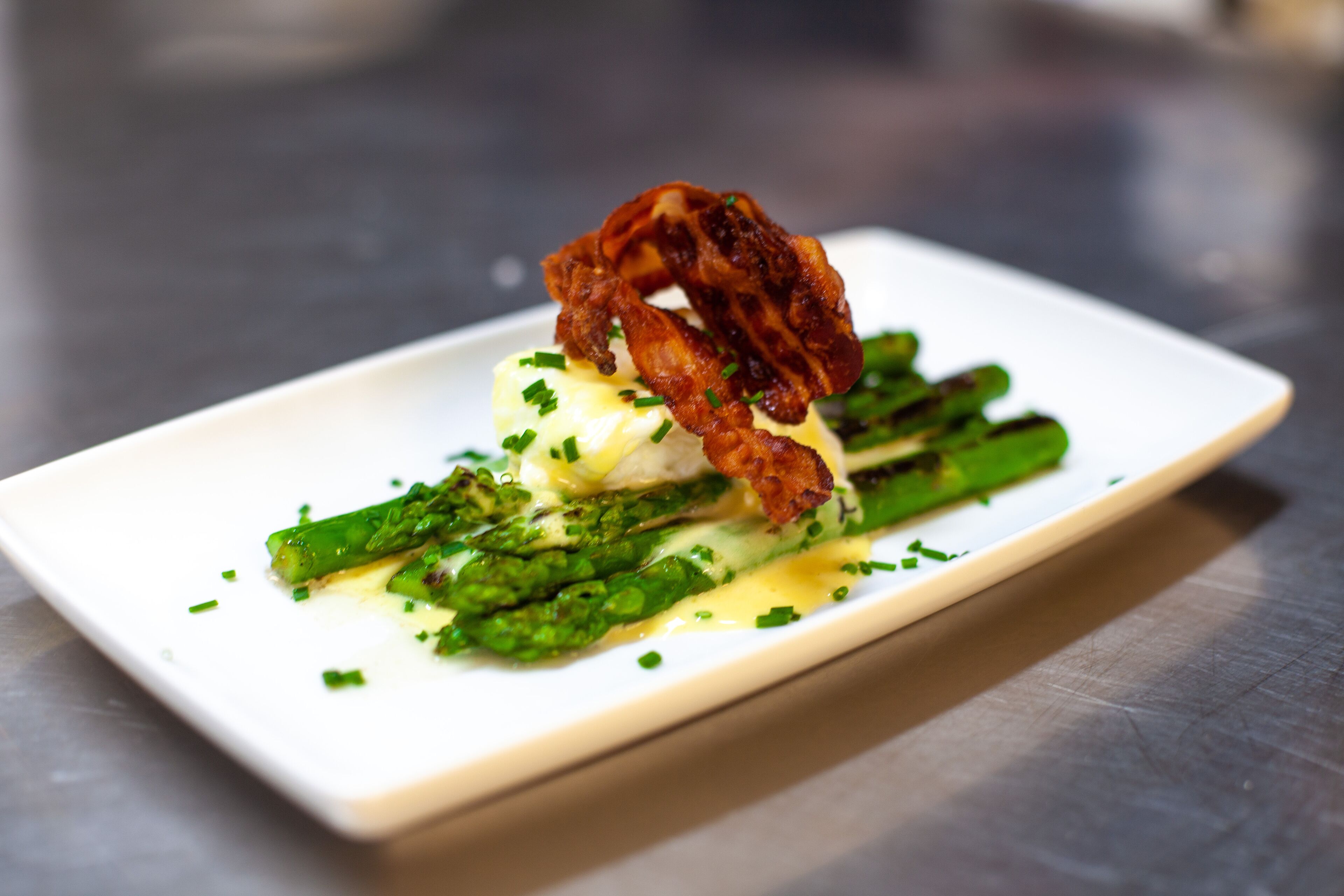 A rectangular white plate with a dish of asparagus, a piece of meat, and a creamy sauce.