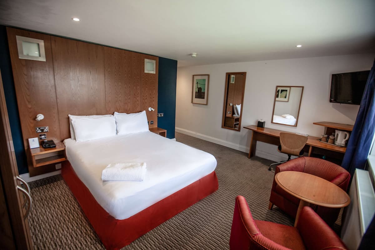 A hotel room with a large bed, a desk, a chair, and a small table.