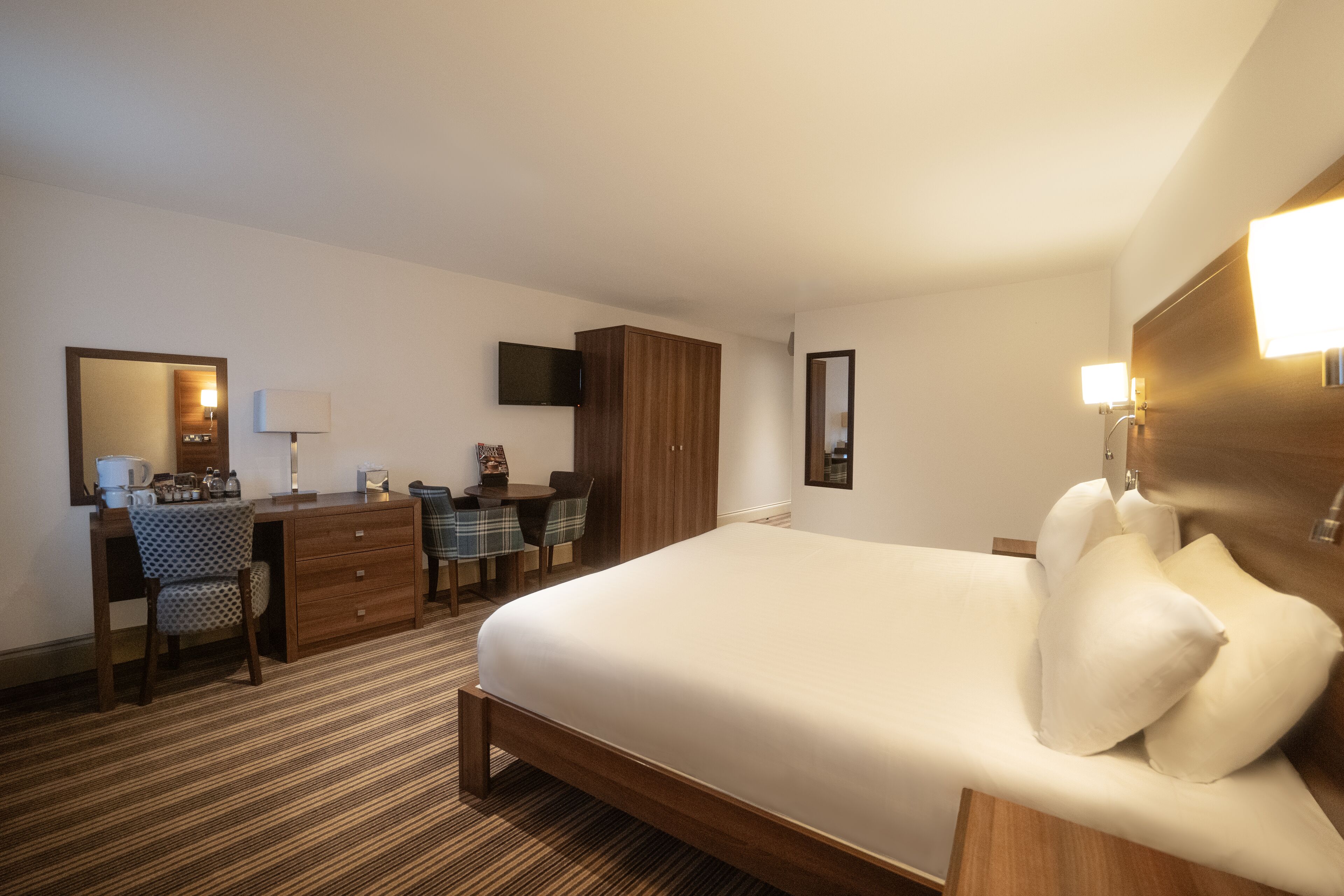 A hotel room with a bed, a desk, a chair, a television, and a wardrobe.