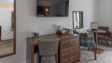 A hotel room with a wooden desk, a chair, a television, a mirror, a small table, and a patterned rug.