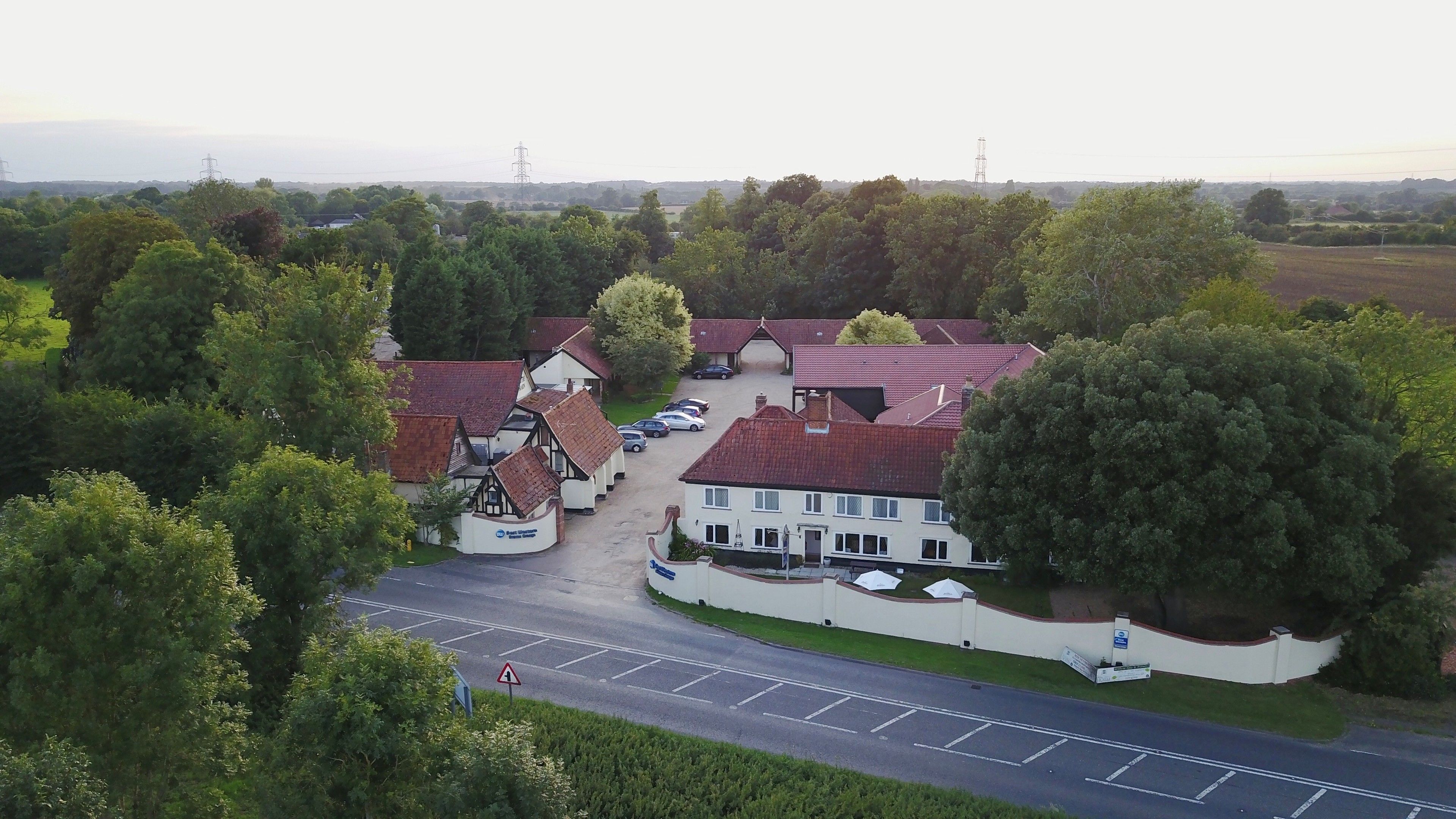 A traditional building with a red-tiled roof, surrounded by lush greenery and a parking area.