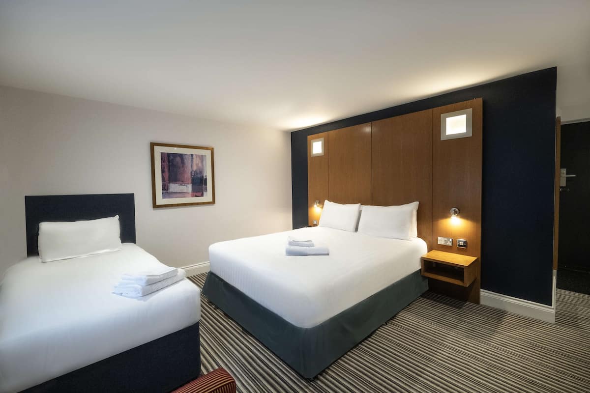 A hotel room with two beds, a framed picture on the wall, and a nightstand with a lamp.