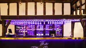 A bar with a neon sign reading "The Tithe Barn" and shelves stocked with bottles. - Best Western Brome Grange (Eye)