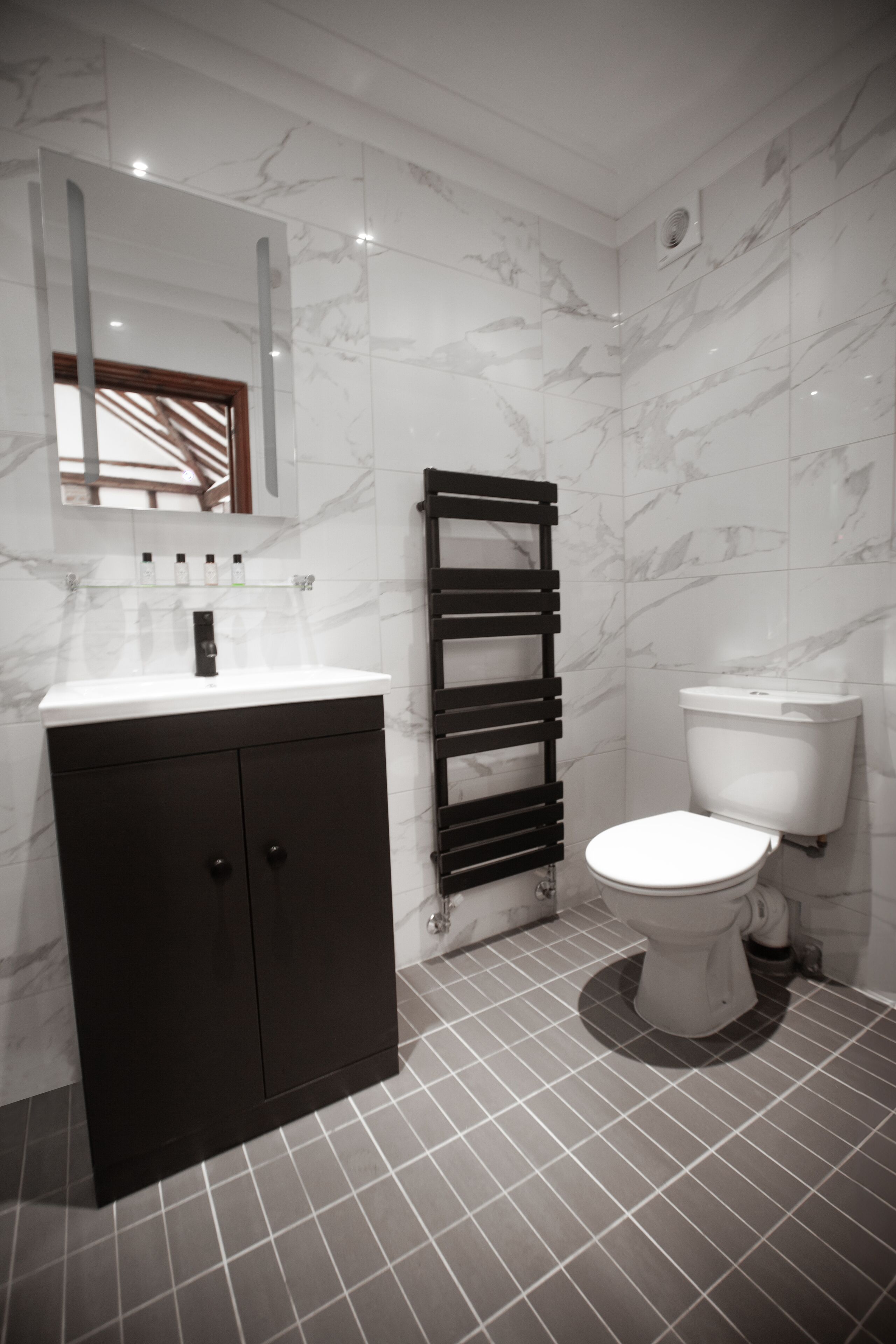 A modern bathroom with a marble wall, a black cabinet, a towel rack, and a toilet.