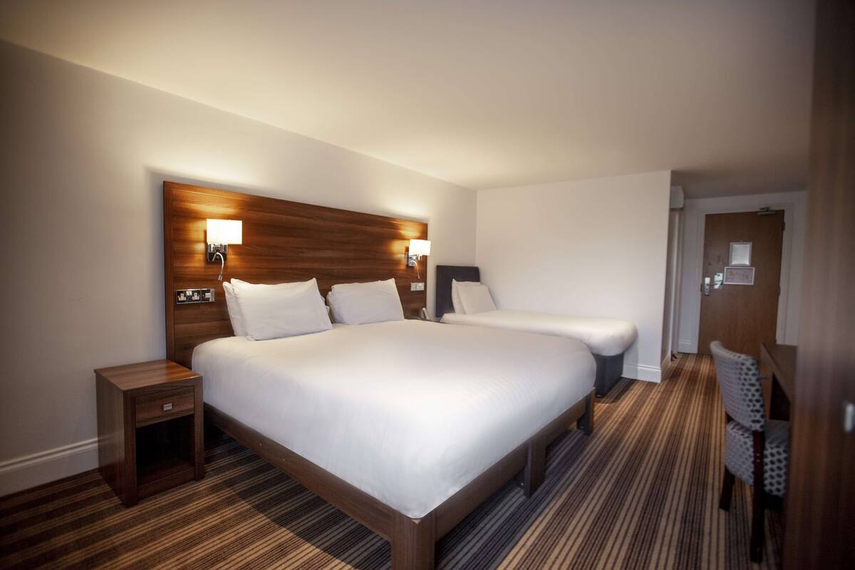 A hotel room with a large bed, a smaller bed, a nightstand, a chair, and a wooden headboard.