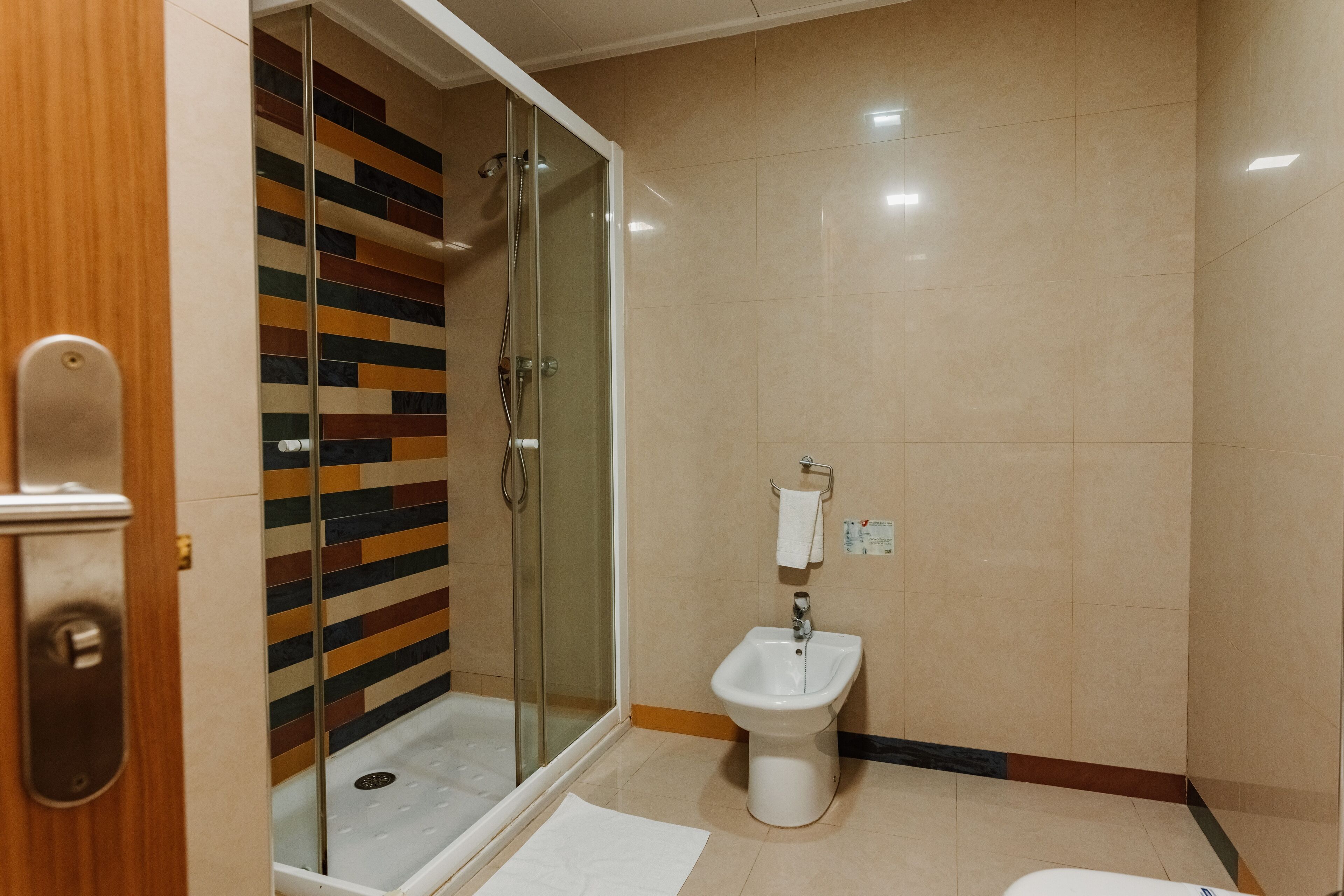 Un baño con cabina de ducha de vidrio, un lavabo pedestal blanco y piso de baldosas.