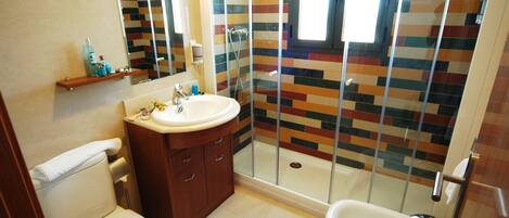 Un baño con ducha, inodoro, lavabo y espejo.
