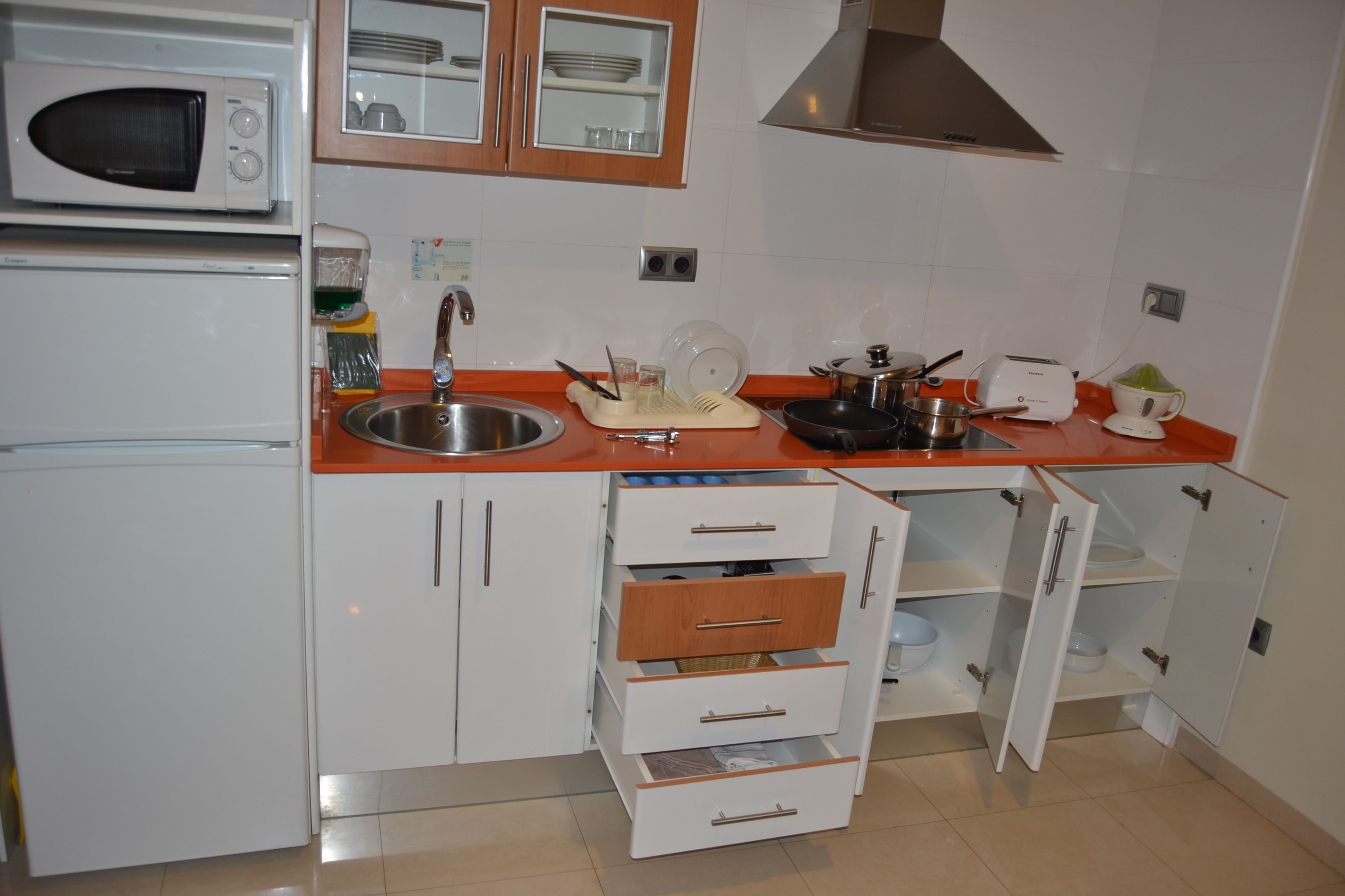 A compact kitchen with white cabinets, a microwave, a sink, and a toaster.
