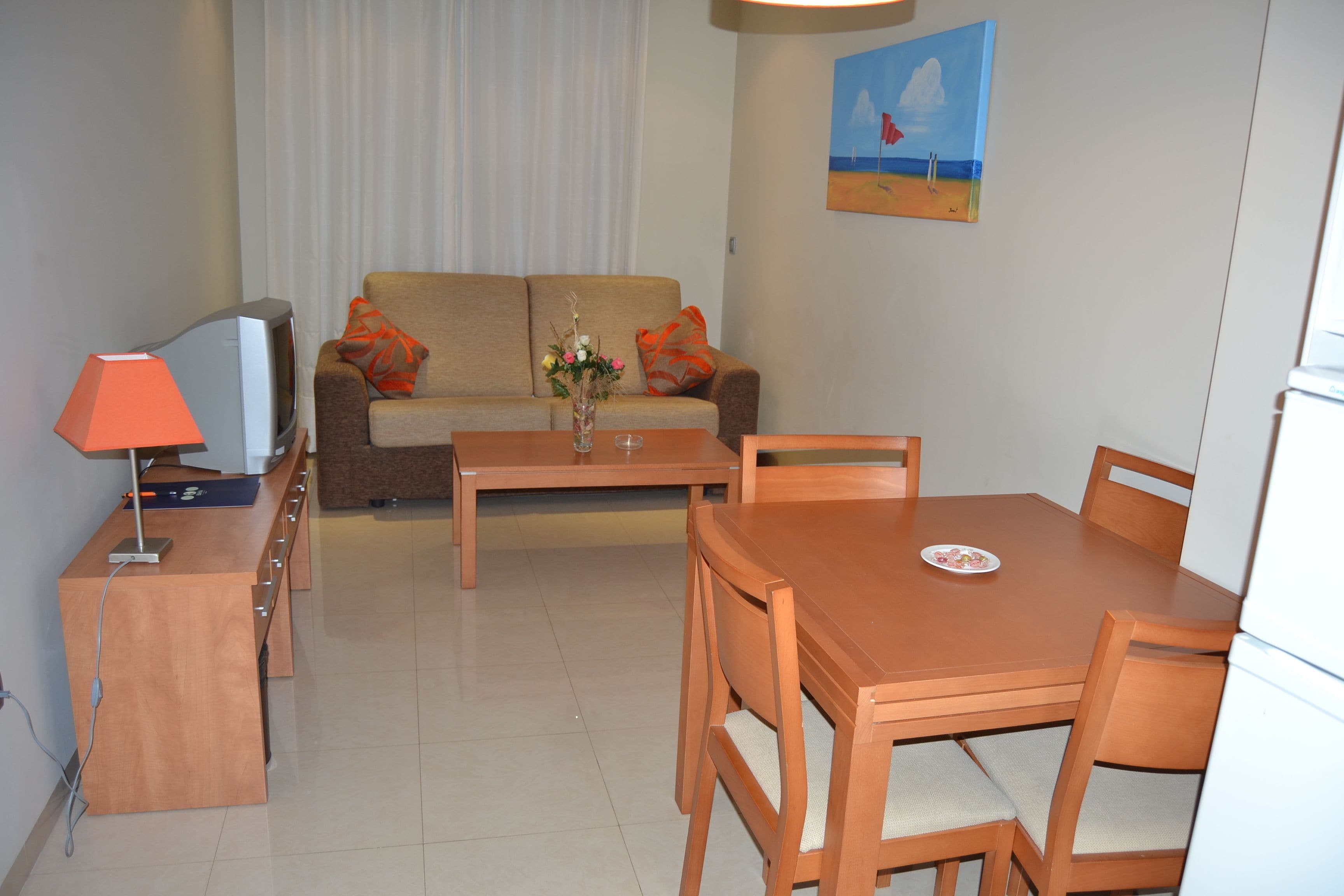 A living room with a sofa, a TV, a table, and a dining area.