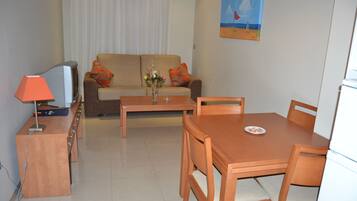 A living room with a sofa, a TV, a table, and a dining area.