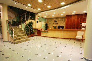A hotel reception area with a marble staircase, a reception desk, and a wooden reception desk. - Aparthotel Bahía (San Pedro del Pinatar)