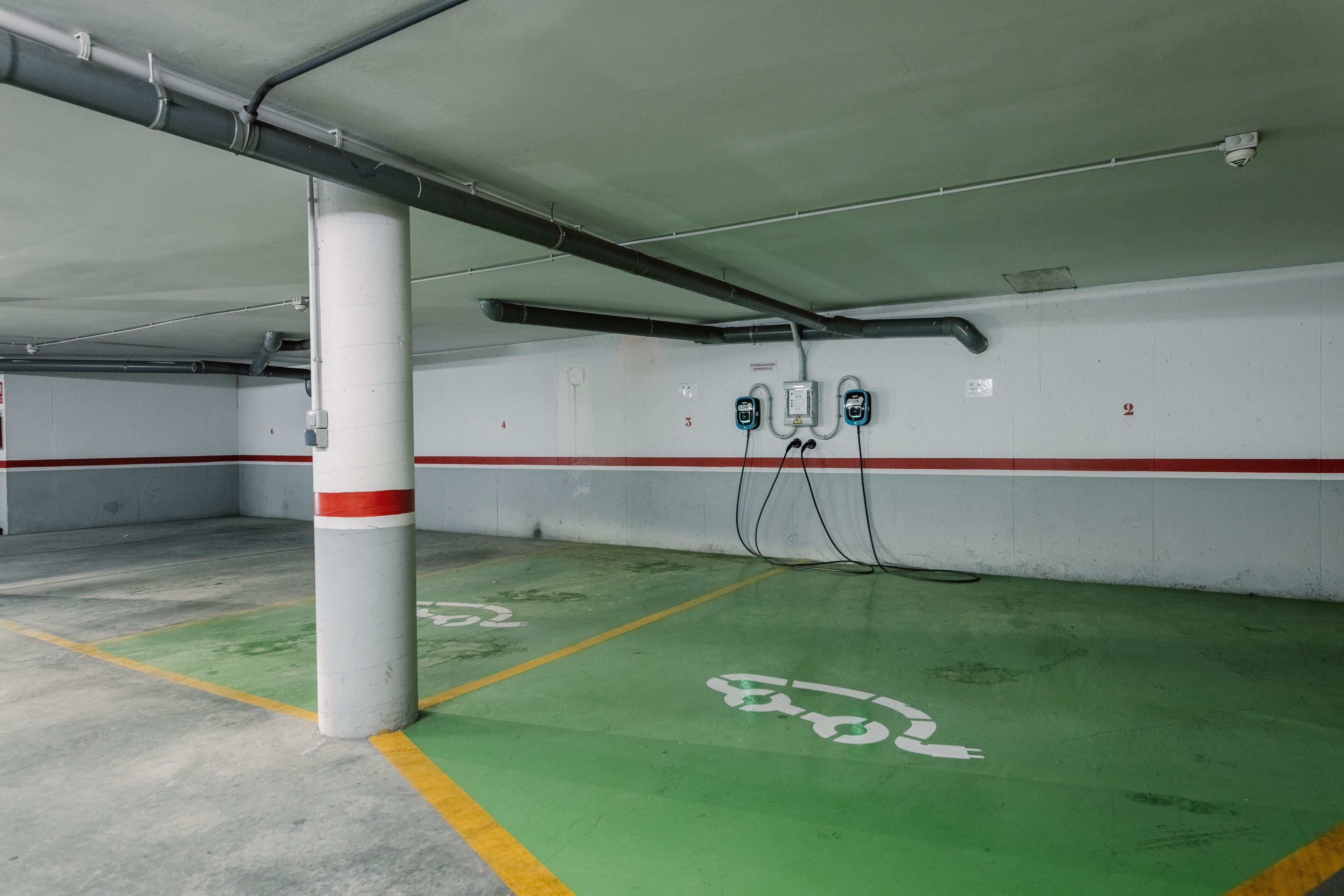 Un parking souterrain vide, avec des pistes cyclables vertes, des piliers blancs et des murs rayés de rouge et de blanc.