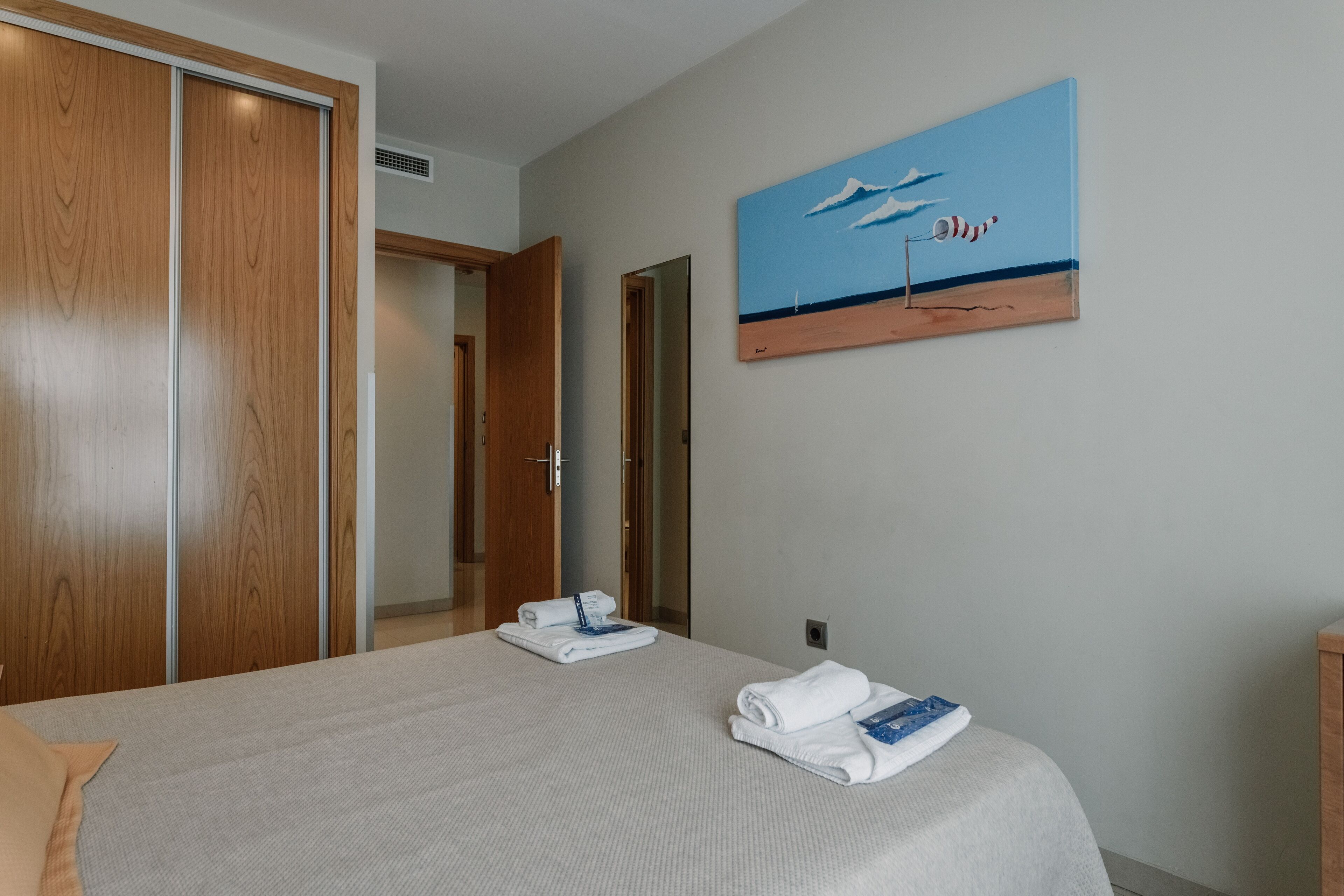 Una camera d'albergo con un letto, un quadro raffigurante una spiaggia e un armadio in legno.