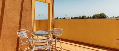 A balcony with a round table and four chairs, a clear view of the sky, and a building in the background.