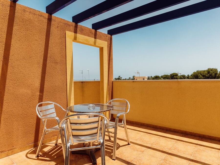 Un balcón con una mesa redonda y cuatro sillas, una vista despejada del cielo y un edificio al fondo.