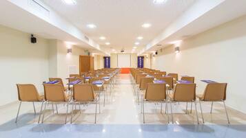 Una sala conferenze con file di sedie e tavoli, uno schermo per proiettore e un podio.