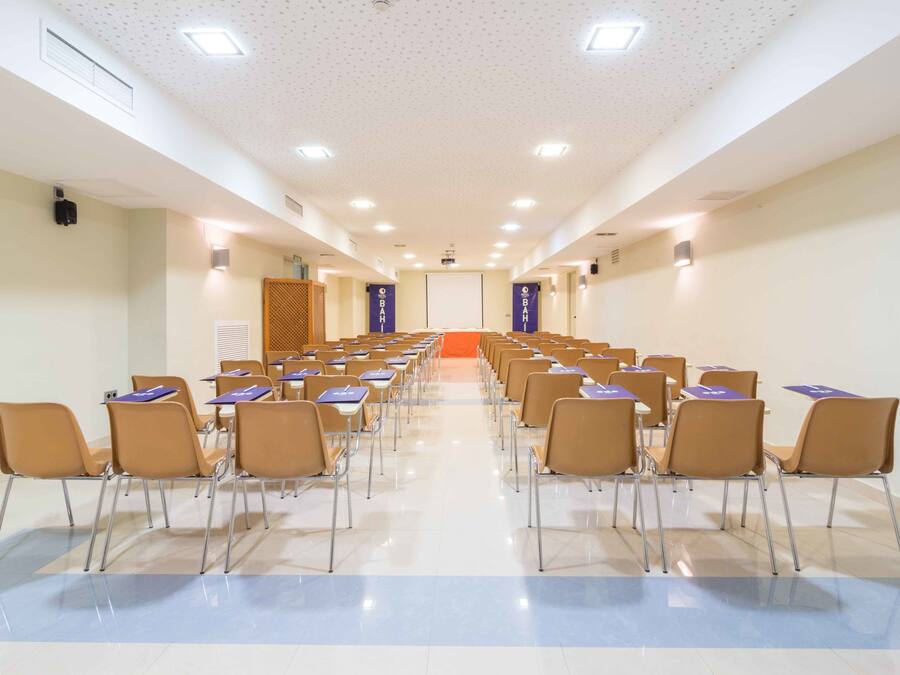 Una sala conferenze con file di sedie e tavoli, uno schermo per proiettore e un podio.