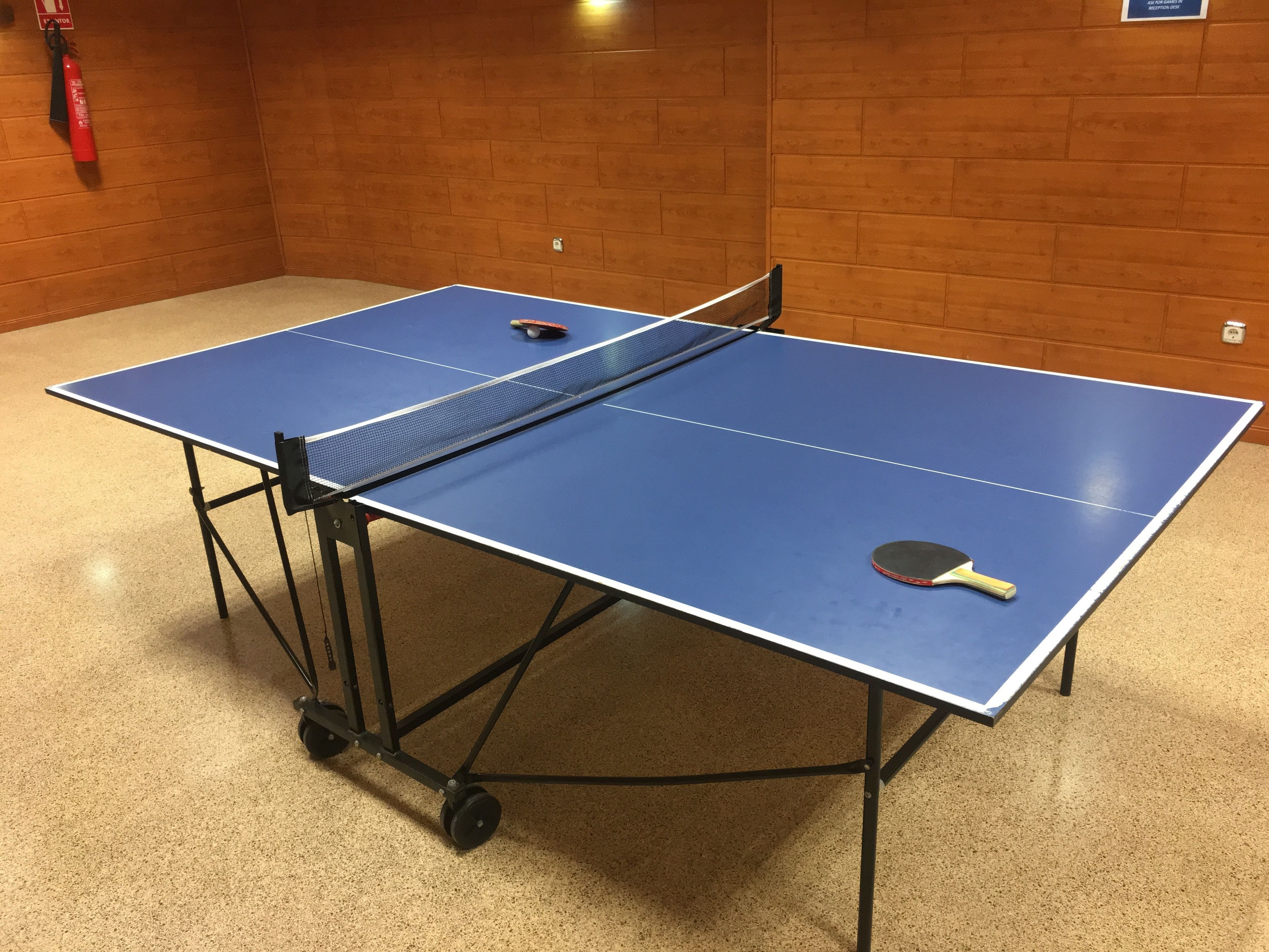 Une table de ping-pong avec un extincteur fixé au mur.