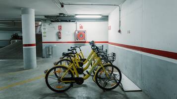 Un estacionamiento con bicicletas amarillas apoyadas en la pared, extintores y una escalera de fondo.