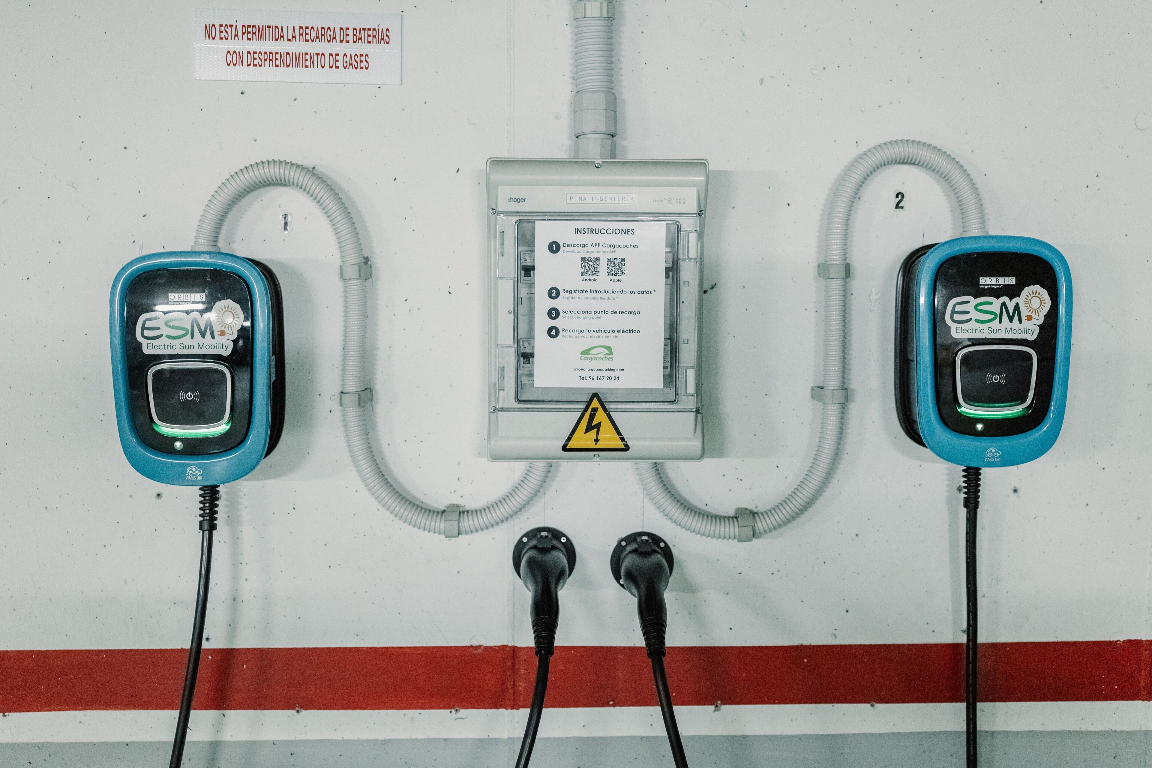 Dos estaciones de carga para vehículos eléctricos, con cables conectados a una caja de distribución de energía.