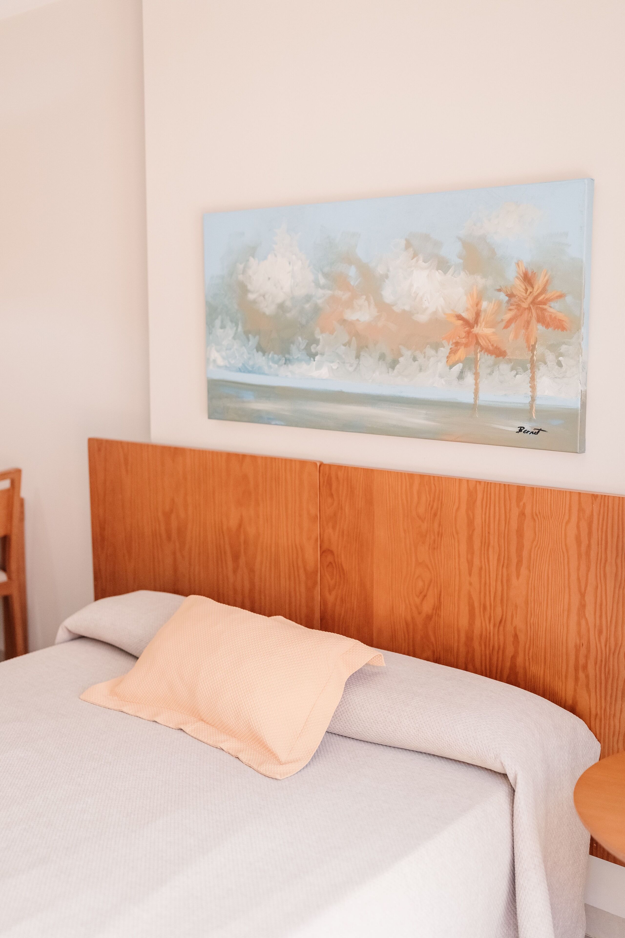 Una cama bien hecha con una colcha de tonos claros y un almohadón color melocotón.