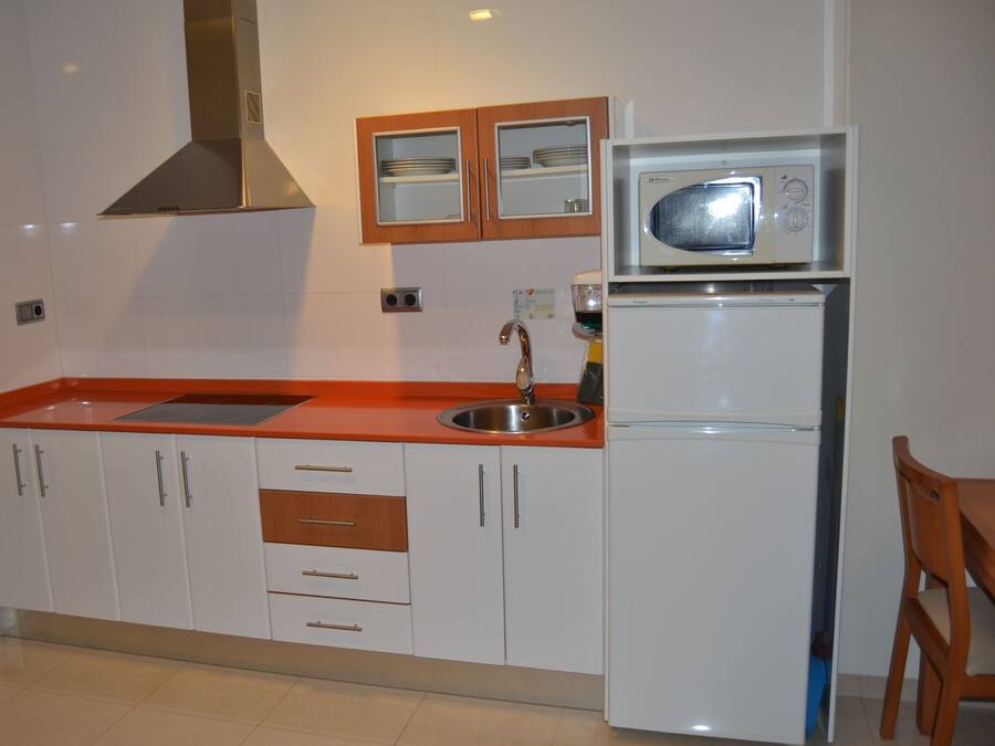 Een keuken met witte kastjes, een rode aanrechtblad, een roestvrijstalen spoelbak, een magnetron en een koelkast.