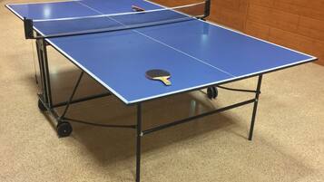A ping pong table with wheels in a room with wooden walls and a fire extinguisher on the wall.