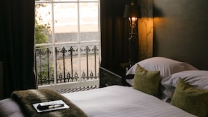 Quarto de hotel com cama, janela com vista, luminária e mesa de cabeceira.
