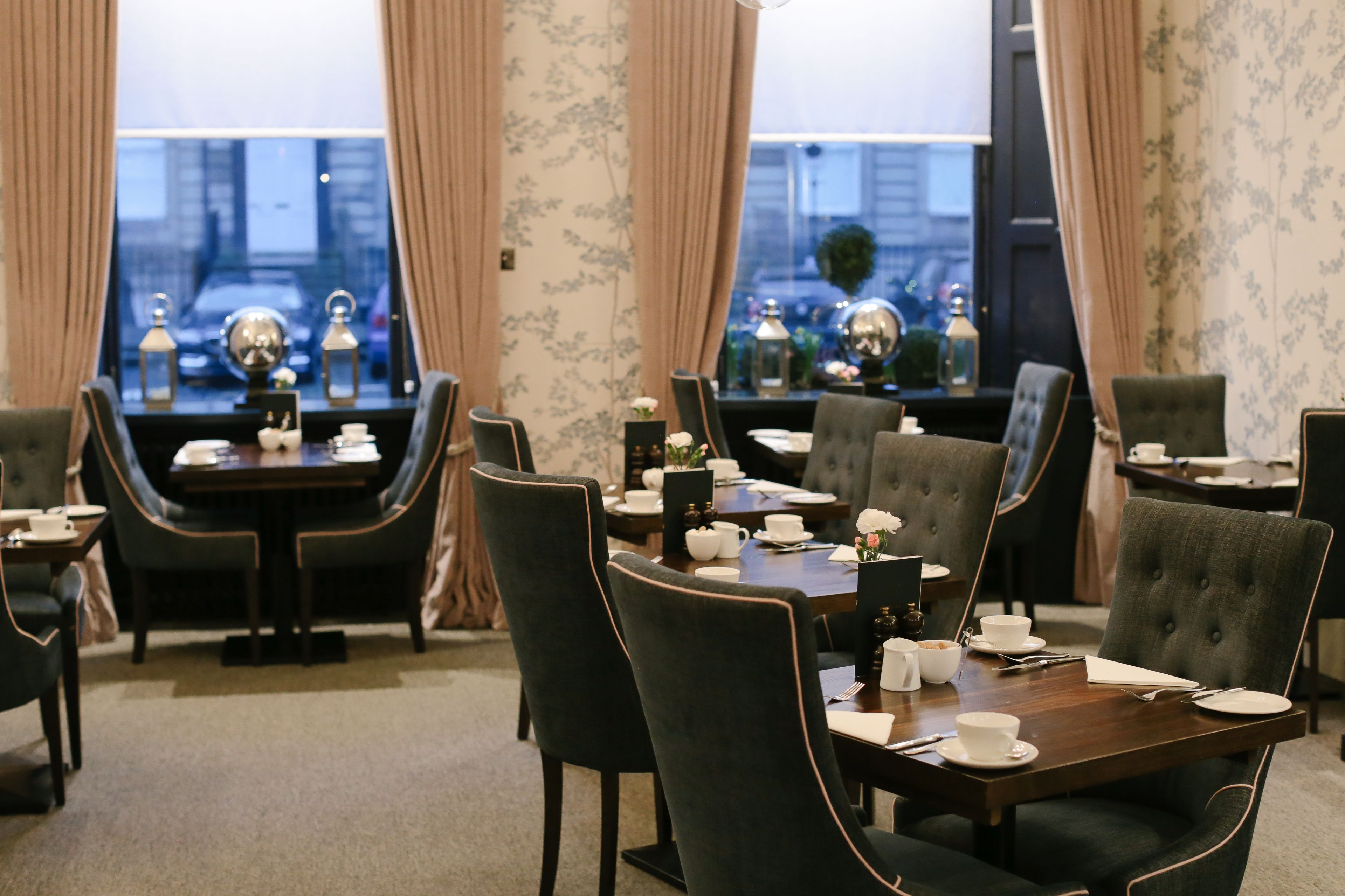 A dining area with a table set for four, surrounded by upholstered chairs, with a view of the city through large windows.