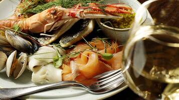 A seafood dish with mussels, clams, and shrimp, garnished with herbs, served on a plate with a fork and a glass of white wine.