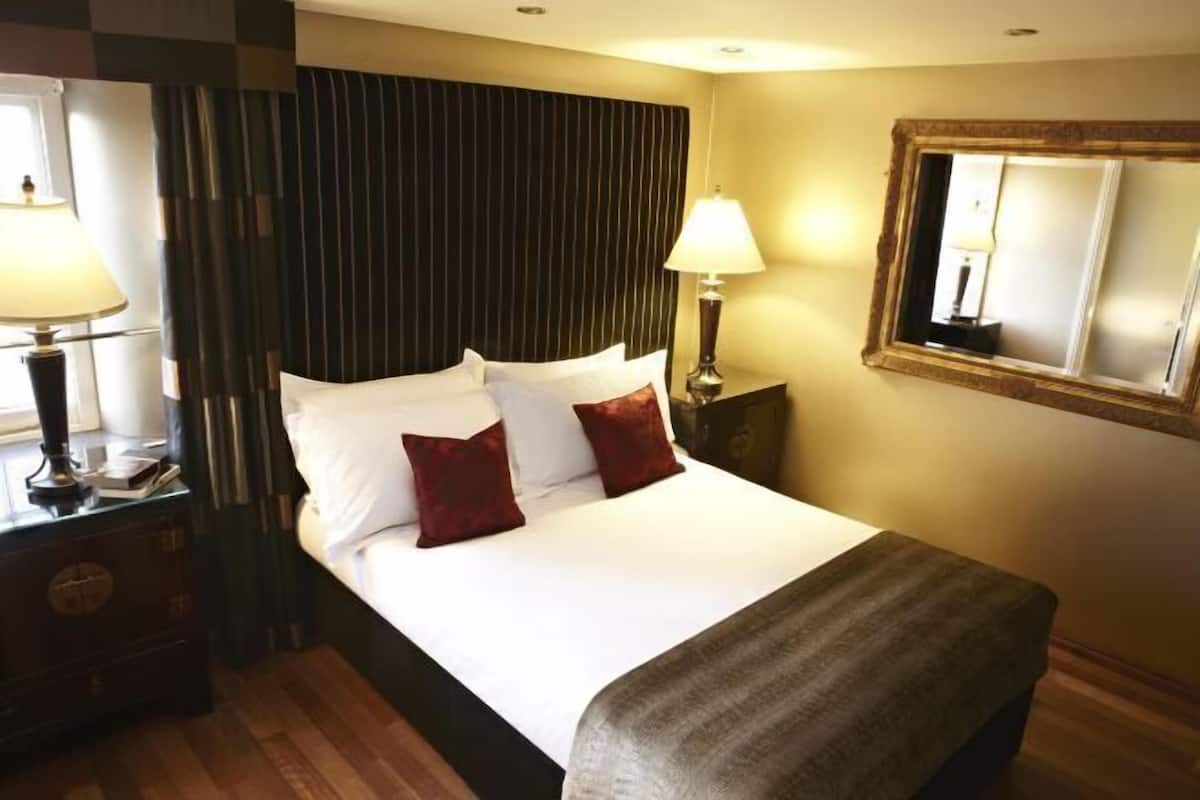 Une chambre d’hôtel avec un lit, des lampes de chevet, une table de chevet, un miroir et une fenêtre.